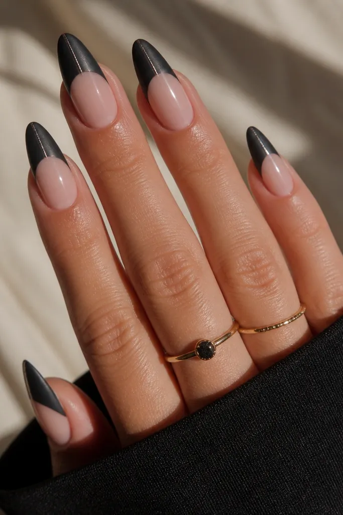 Almond nails with a matte black French tip. The cat-eye stripe is glossy and bright, running vertically through the black, while the rest of the black area stays matte. Nude base shows clearly between.