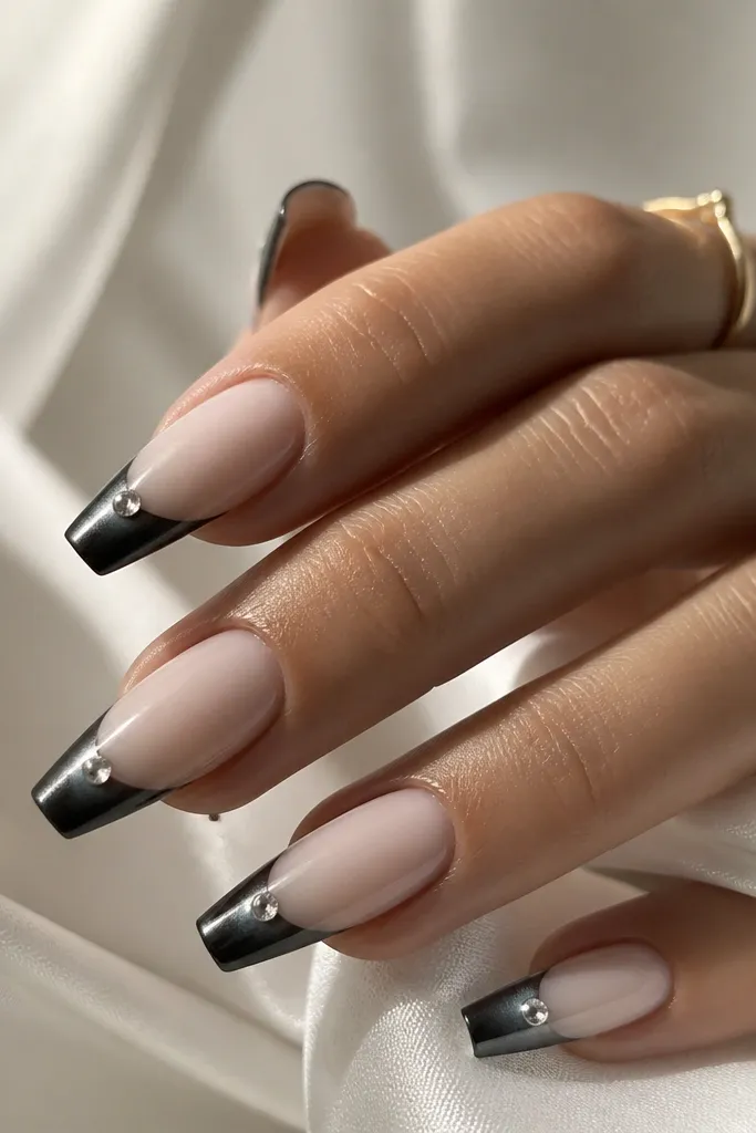 Coffin nails with nude base and black cat eye French tips. A small clear crystal sits in the center of the tip area, like a tiny bezel, catching light right where the cat-eye stripe runs.