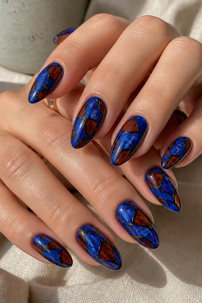 Ten glossy medium almond nails. The base is royal blue with a subtle marbled look. Over that, tortoise shapes are drawn in dark brown, then each shape is outlined with a fine black liner line. The outlines are crisp and create a stained-glass effect.