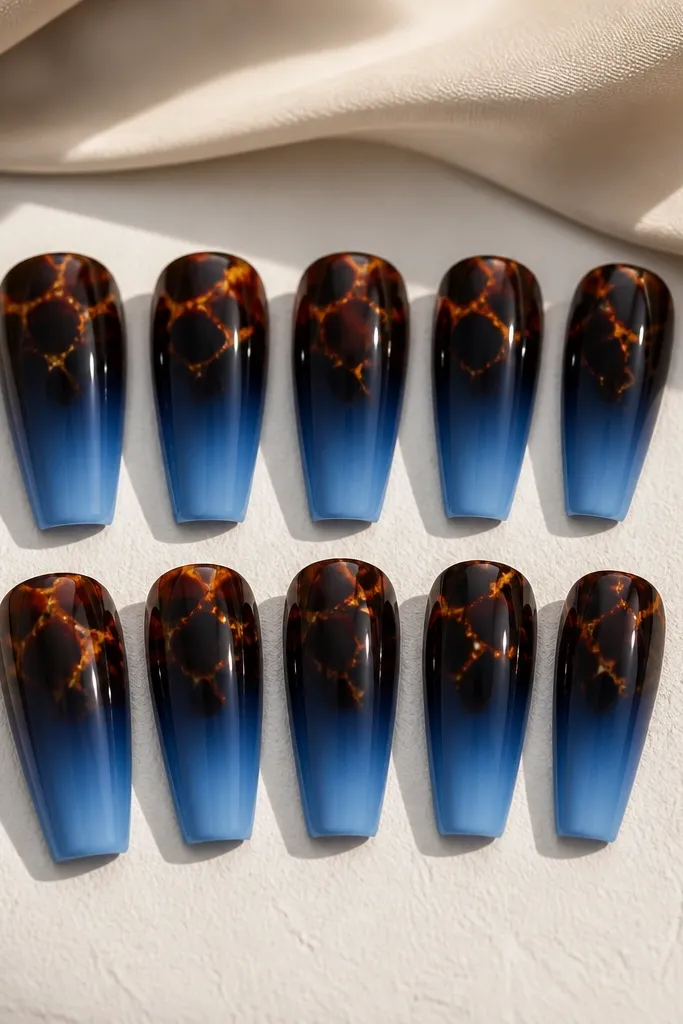 Ten glossy coffin nails. The base fades from deep navy at the cuticle to lighter blue toward the middle and tip. The tortoise shell pattern is concentrated at the top third of each nail, with warm brown shapes and thin amber highlights.