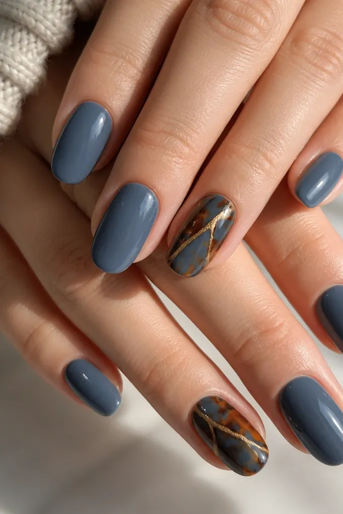 Ten glossy nails with a solid slate-blue base on most fingers. On two accent nails (ring fingers), there is full tortoise shell in blue and warm amber, with wavy veins and shell shapes. The accent nails look layered and slightly more detailed than the rest.