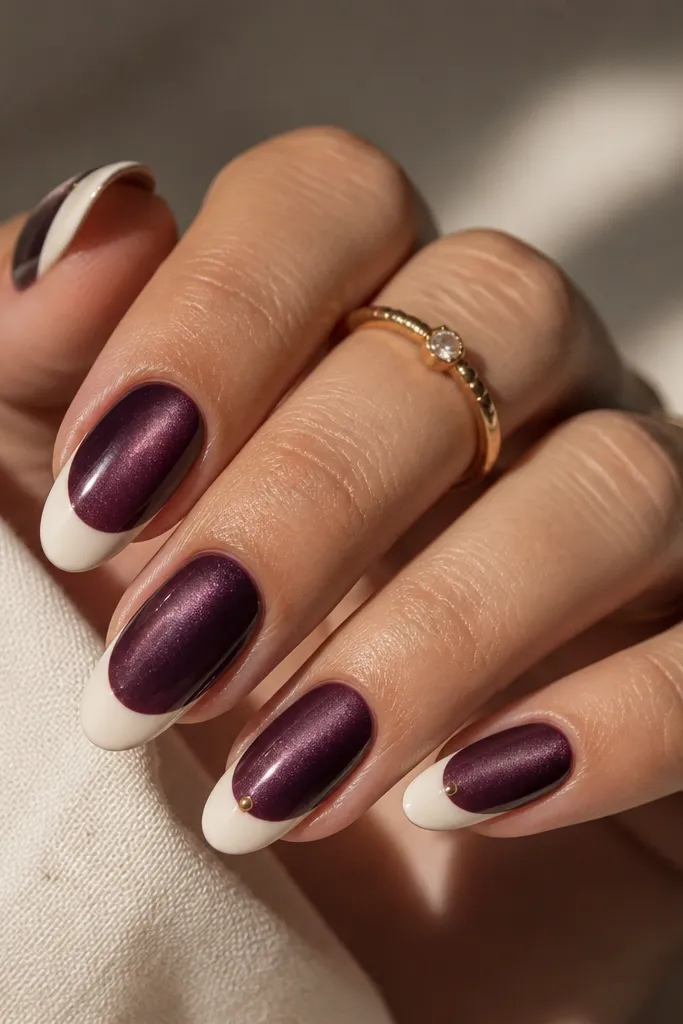 Cat-eye plum nails with a bright cream French tip. On the ring fingers, there is one small gold dot centered at the border where the cat-eye meets the French tip.