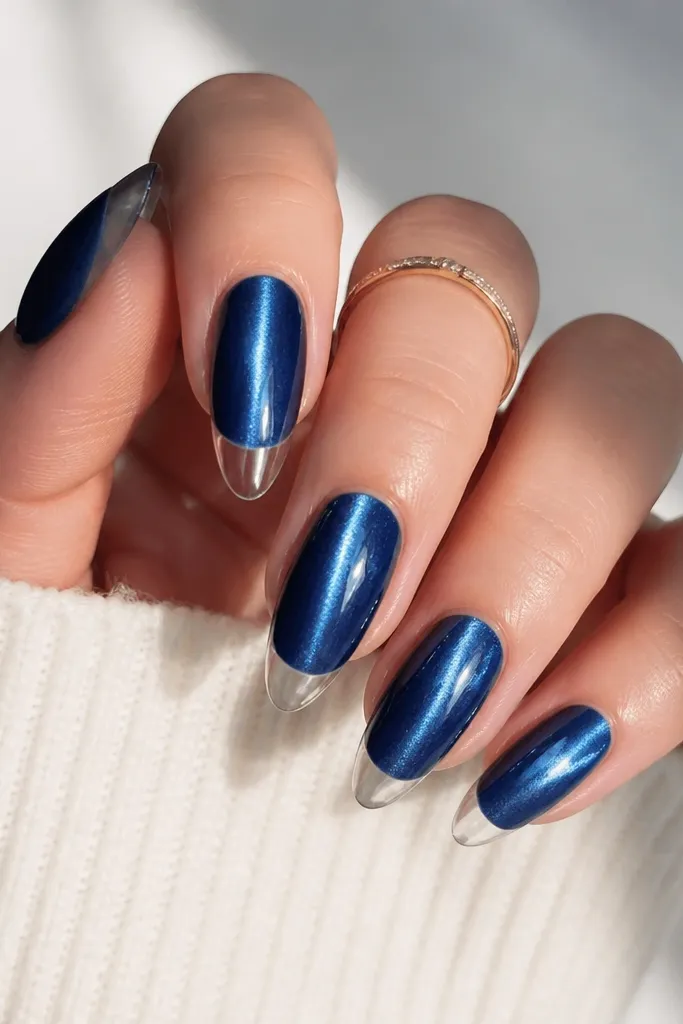 Sapphire blue cat-eye nails with a strong vertical shimmer line. The French tips are clear or sheer with a glossy, glass-like look rather than opaque white.