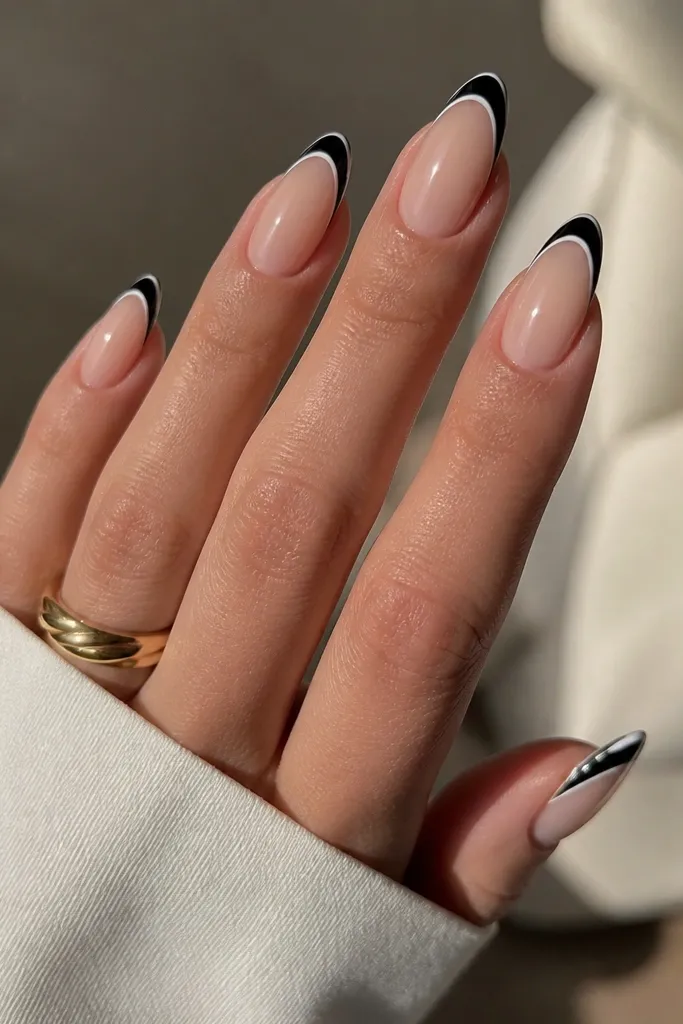 Almond nails with a glossy nude base. The French tips are painted black in a clean curved line, and around the black tip there is an ultra-thin white outline like a border. The outline is crisp and evenly spaced across all nails.