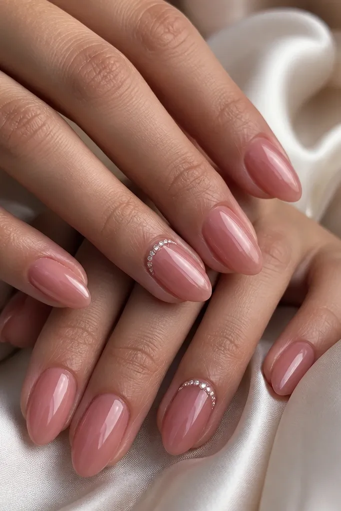 Medium almond nails with a warm rose jelly base. At the cuticle area on two accent nails per hand, there are tiny half-moon shapes made of micro rhinestones that curve along the nail. Other nails are plain glossy rose jelly with a subtle natural shine.