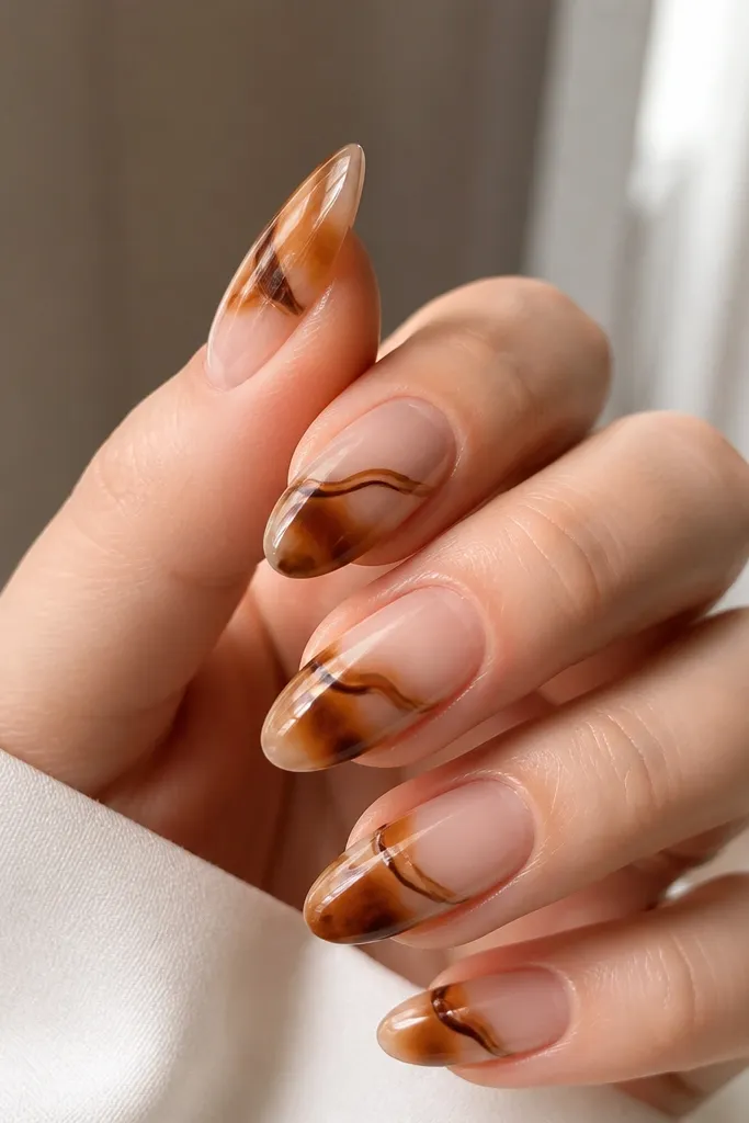 Almond nails with a sheer clear base. Caramel tortoise patches and thin brown lines sit in the middle and lower half, leaving the upper third mostly transparent. The nails have a high-gloss finish.