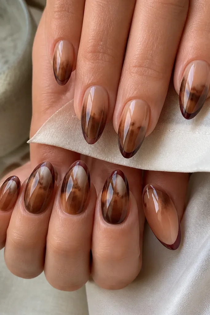 Almond nails with a smoky nude-to-caramel gradient. The tortoise pattern shows as soft marbling in the mid section with darker edges. The tip area has a thin burgundy edge line, like a reverse French accent, all under a high-gloss finish.