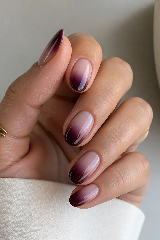 Short oval nails with a nude base. The tips fade into a deep blueberry jam color, blended softly so there's no hard line at the transition. Glossy finish throughout.