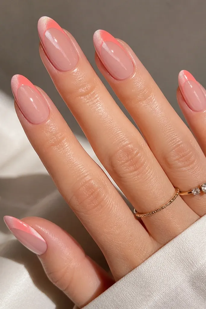 Almond nails with a soft coral-pink base. French tips are coral pink arcs, and the cat eye effect shows a bright stripe that shifts slightly to one side when the light hits. The stripe looks like it moves subtly across the tip. The finish is glossy and the lines are crisp.