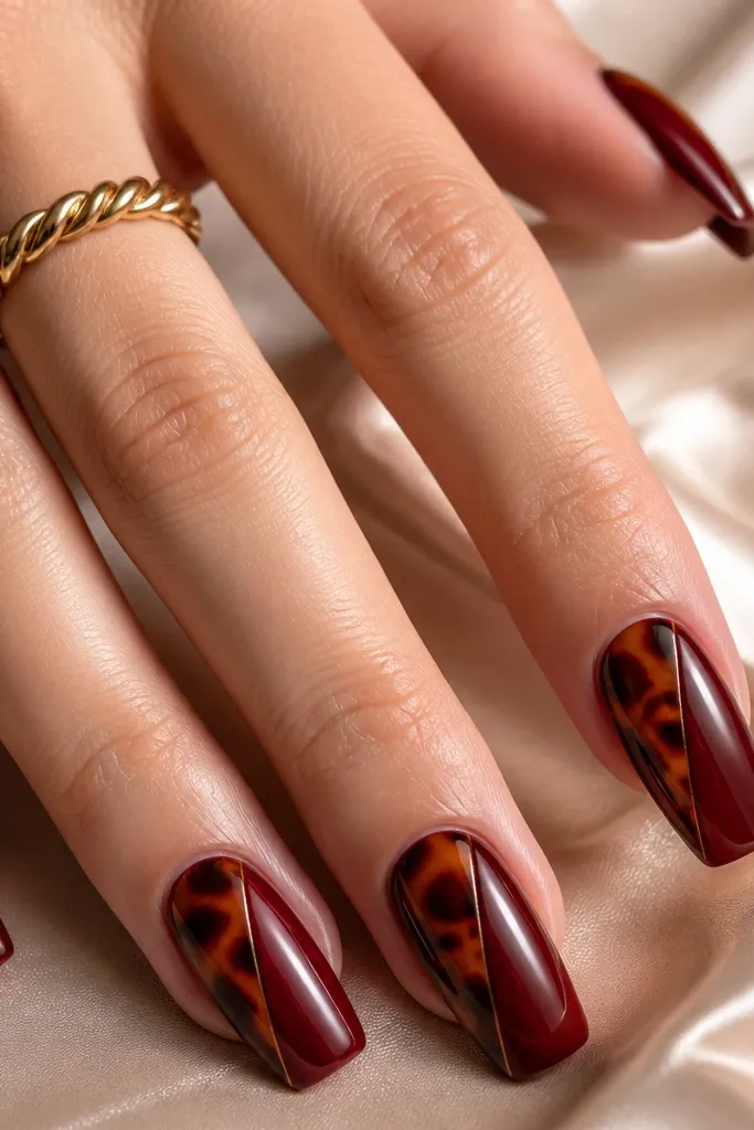 Long squoval nails split diagonally. One side is tortoise shell, the other side is a smooth oxblood red. A thin oxblood outline crisply separates the two halves, glossy finish.