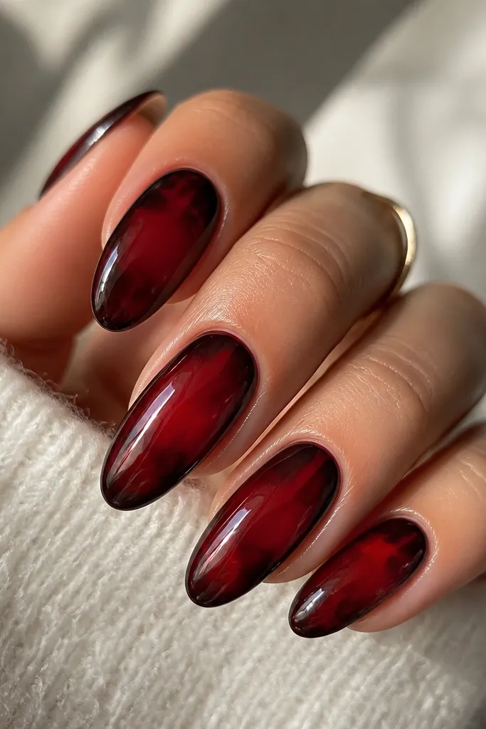 Glossy ruby-red nails in a long oval shape. Each nail has a tortoise pattern that looks like a dark black-brown rim around the edges, with lighter maroon shell shapes inside. The center stays ruby-clearer while the perimeter looks framed.