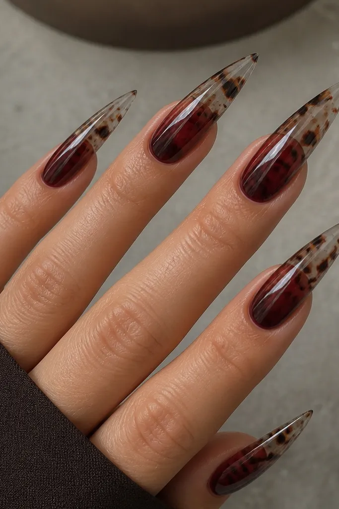 Long stiletto nails with a smoky fade from transparent at the tip to deep red near the middle. Brown shell spots and darker maroon blobs float like tortoise islands, with subtle black-brown speckling. The nails are glossy and light reflects off the smoke gradient.