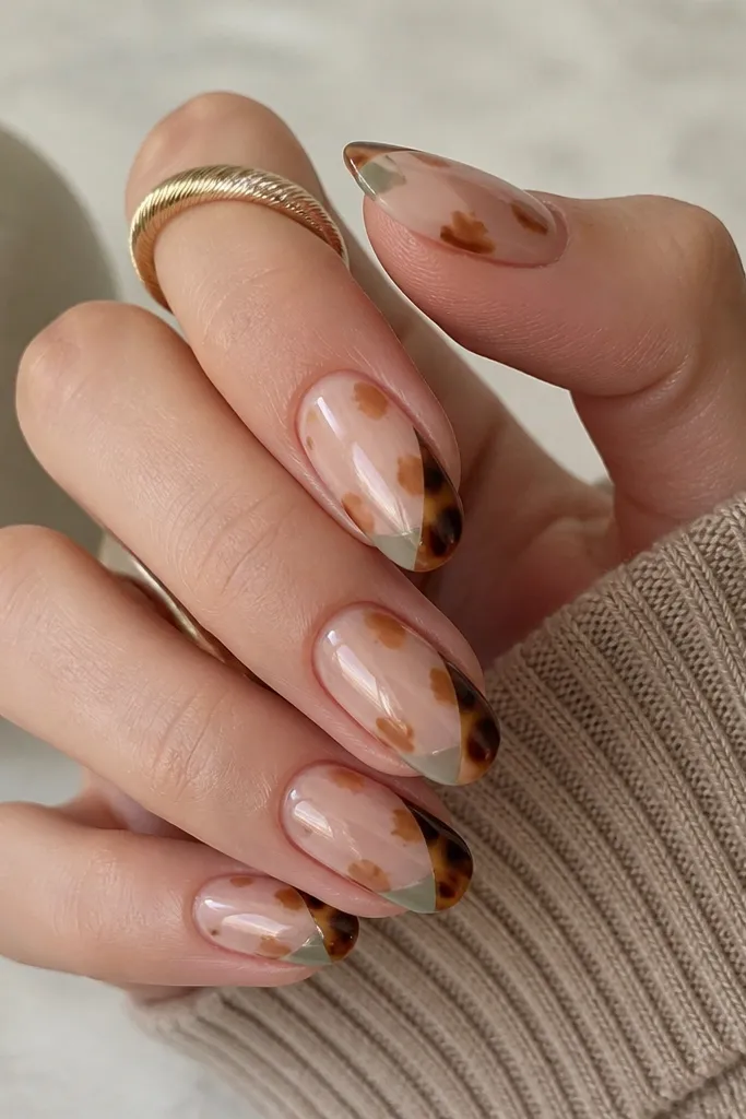 Slightly longer oval nails. The base is nude with tortoise shell blotches in taupe and caramel. The French tip is a tortoise gradient that's darker near the outer edges. In one corner of the nail near the tip, there is a small negative space triangle filled with sage-taupe (not fully brown), creating a modern corner detail.