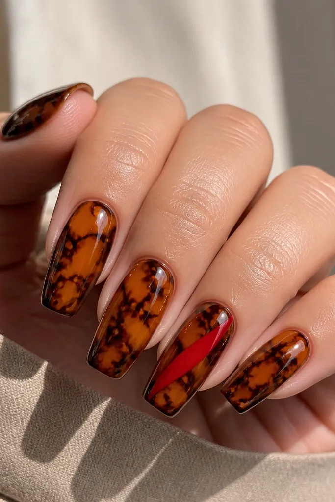 Medium coffin nails. Tortoiseshell pattern is warm amber and chocolate with thin dark lines. One nail has a bold blood-red diagonal slash from lower left near the sidewall to upper right near the tip; the slash is glossy and sharply edged.