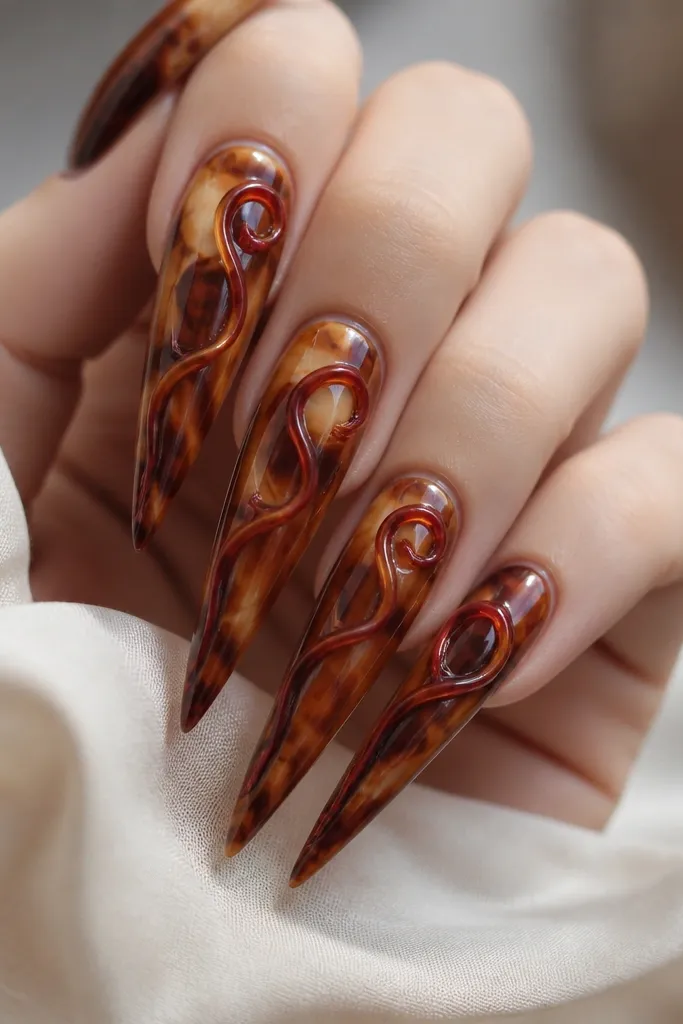 Long stilettos. The tortoiseshell forms a flowing swirl from base to tip in amber and chocolate tones. One side of the nail has a glossy red loop that follows the swirl direction, like a ribbon curling near the center.