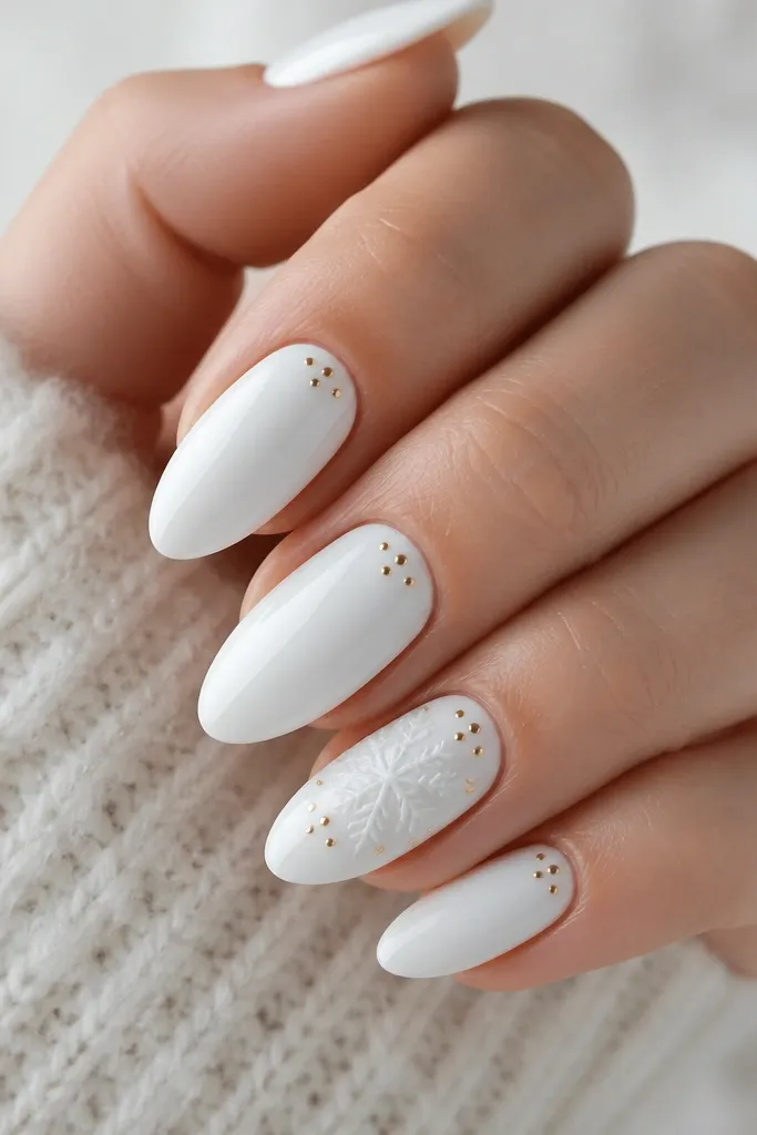 A set of medium almond nails in glossy white. On the ring finger there is a delicate white-on-white raised snowflake with a few tiny gold dots around it. Other nails have scattered small gold dot accents near the cuticle.