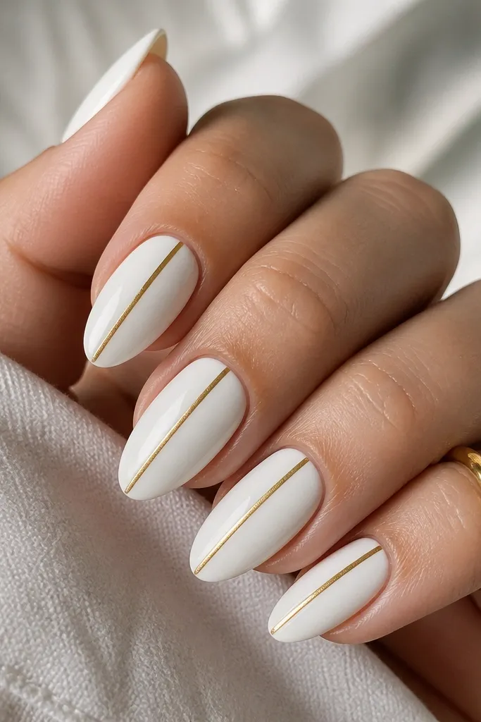 Medium almond nails painted solid opaque white. A single straight gold stripe runs down the exact center of each nail from cuticle area to near the tip, with glossy finish.