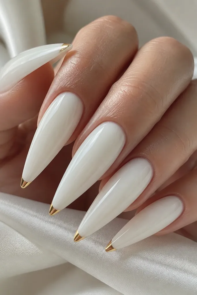 A set of long white stiletto nails with a glossy milky white base. Each nail has a very thin gold French line right at the very tip, like a straight 1-2 mm band. The gold is metallic and crisp, with clean edges and a high shine finish.