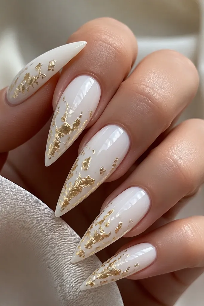 White stiletto nails with small scattered gold foil confetti pieces suspended under a clear glossy dome. The confetti appears concentrated near the lower middle and disperses toward the tip. The surface looks smooth like glass, with the foil glittering under the top layer.