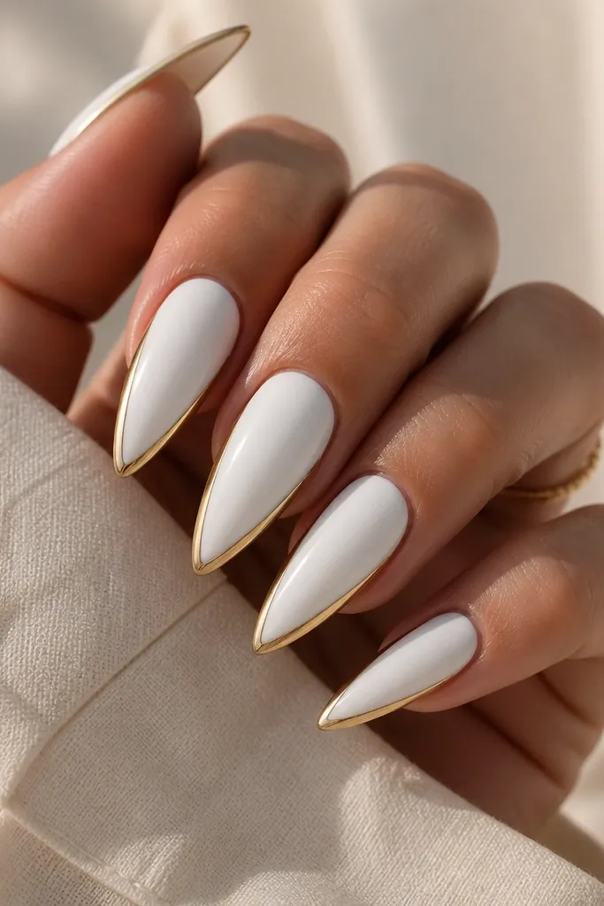 Glossy white stiletto nails with a thin metallic gold line that frames the nail perimeter. The gold outline traces the sidewalls and curves along the tip edge, leaving the center fully white. The outline is crisp and reflective, with no gold fill inside the frame.