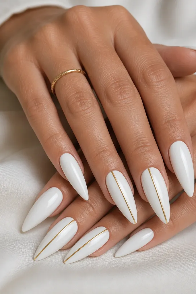 A coordinated set where most stiletto nails are glossy white. Alternating nails have a thin gold accent line running vertically or diagonally near the center. The gold lines are crisp, reflective, and placed with consistent spacing across the accent nails.