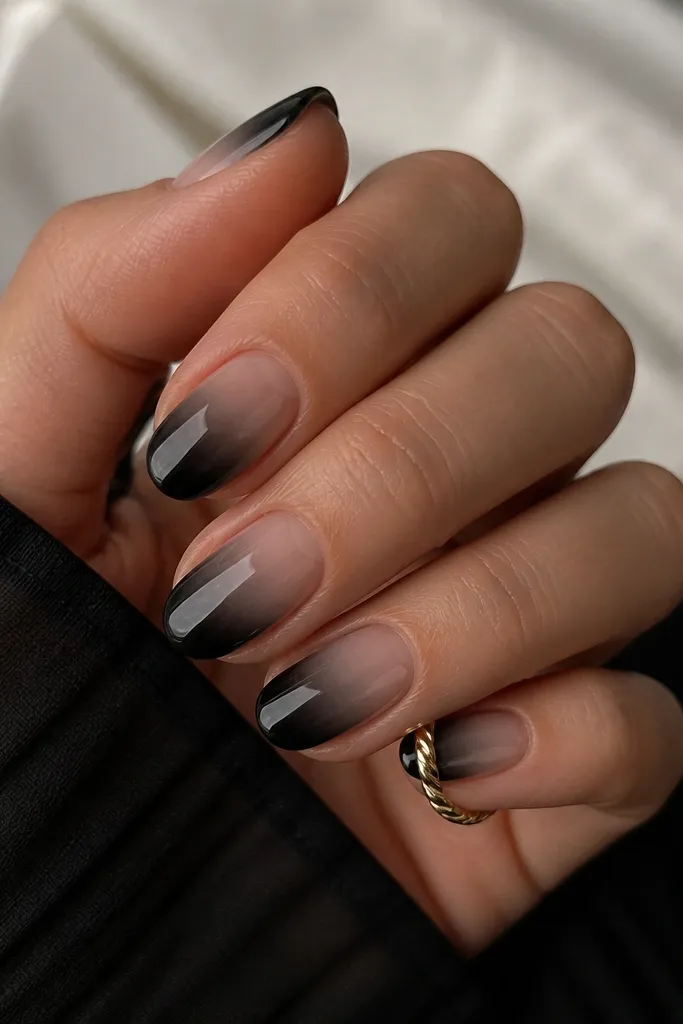 Short oval nails with a smoky black gradient that is heaviest near the tip and fades into a sheer nude near the base. The finish is glossy, with a soft smoky haze and clean edges.