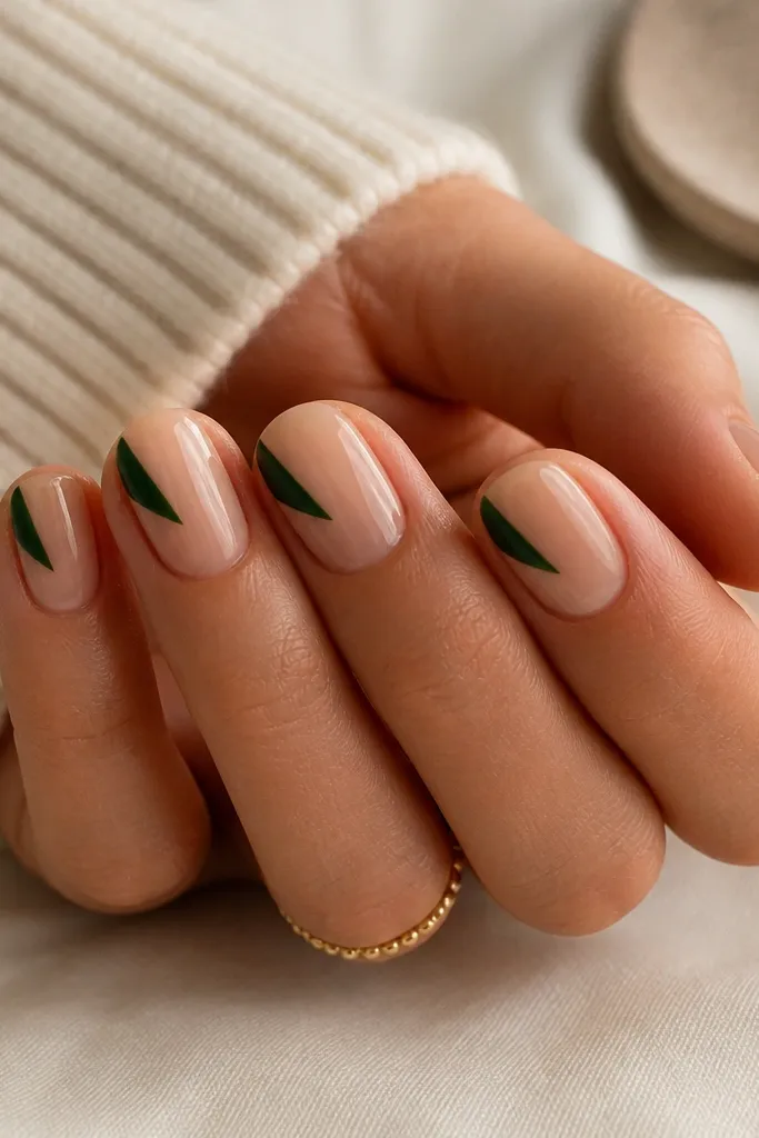 Short oval nails with a nude base. Each nail has a single evergreen green triangle at the side near the tip, with crisp edges and a glossy finish.