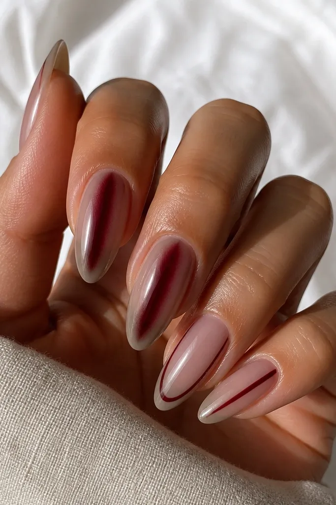 Almond nails with taupe nude base, burgundy cat eye stripe centered. French tips are taupe, and two accent nails show thin burgundy lines along each side of the nail near the tip. Glossy finish.