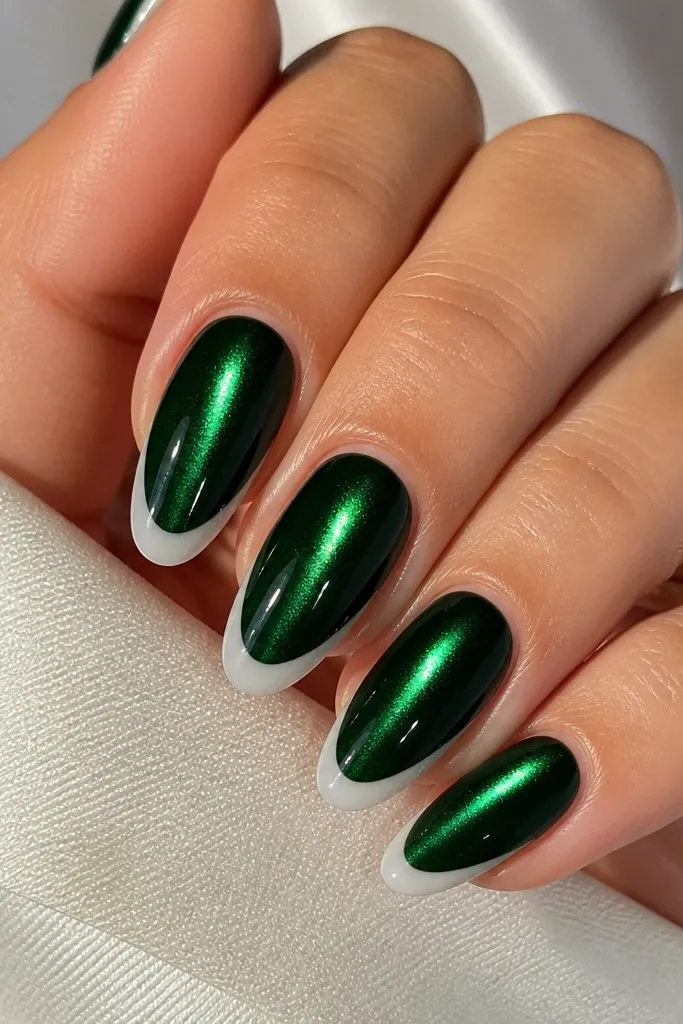 Close-up of almond nails: deep emerald magnetic cat eye base with a bright vertical shimmer streak, and a smooth milky white French arc that hugs the tip line. Glossy top coat, no rhinestones, natural cuticle line.