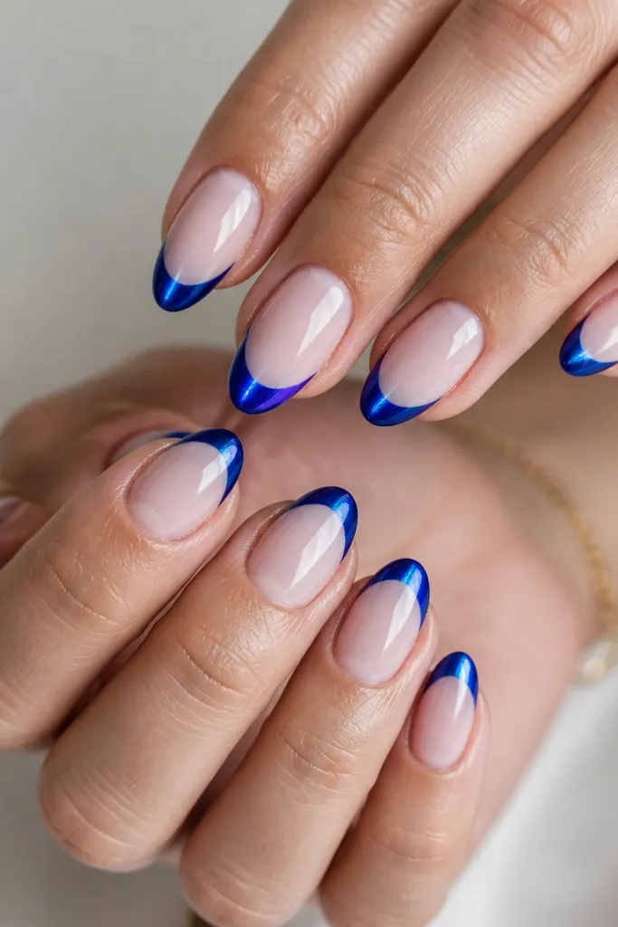 Short almond nails with a milky nude base. The French tips are cobalt blue cat eye gel with a bright vertical light streak running down the tip center. The tips have a crisp smile line and a glossy, mirror-like top coat.