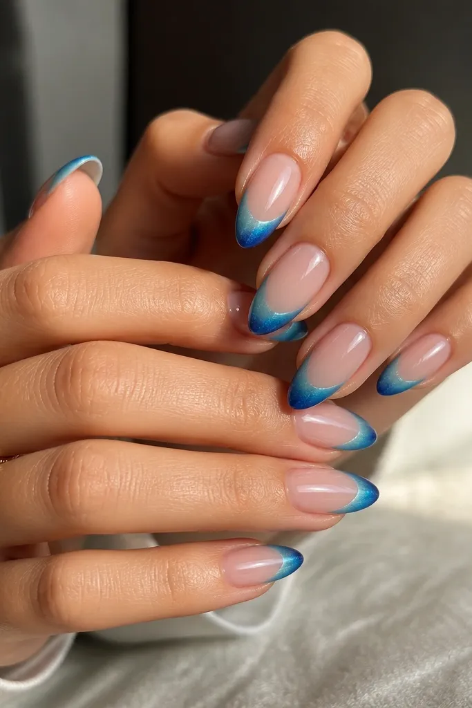 Medium almond nails with a nude base. French tips fade from teal at the smile line into deeper blue at the free edge. The cat eye streak is visible and bends slightly as the gradient changes, with high shine top coat.