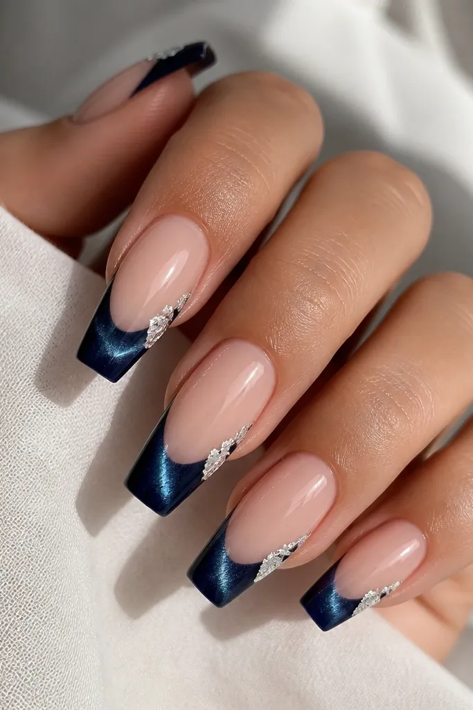 Coffin nails with a sheer nude base. French tips are midnight blue cat eye with a bright central streak. A few tiny silver foil flakes are placed near the outer corners of the tip, and the nails are glossy.
