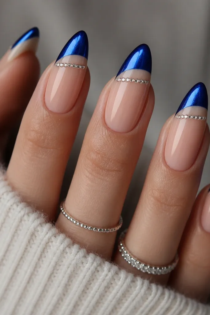 Long almond nails with a nude base. French tips are royal blue cat eye with a bright stripe. A straight micro rhinestone line runs a few millimeters below the smile line across each nail, all in silver tones.