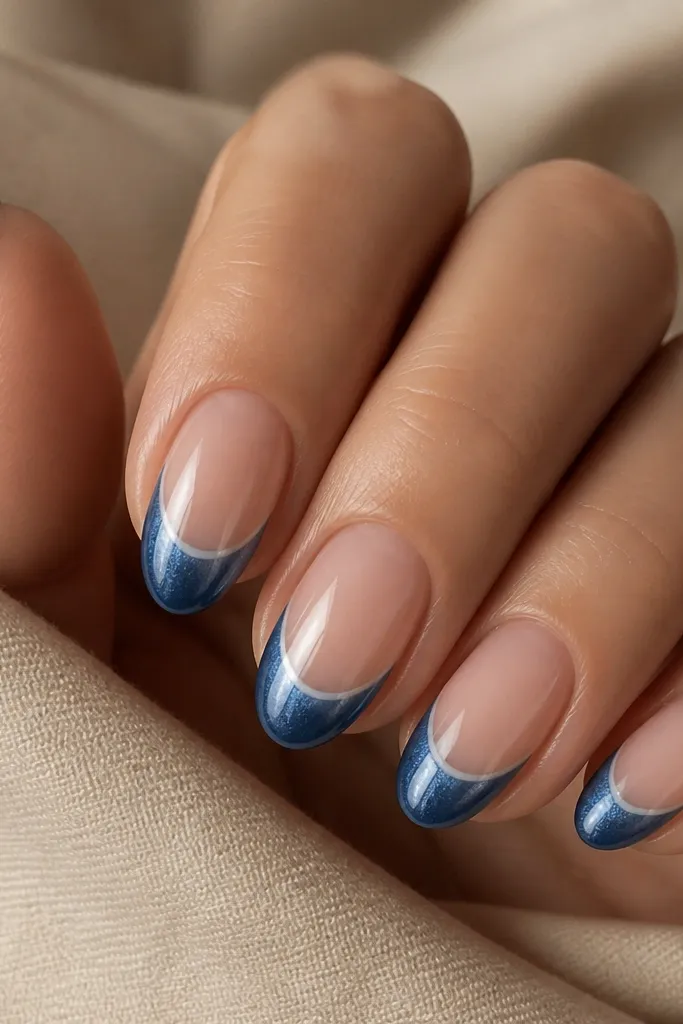 Short almond nails with a nude base. A denim blue cat eye French tip forms a curved U-shape, leaving a small negative space gap at the smile line. The magnet streak runs down the center of the blue portion.