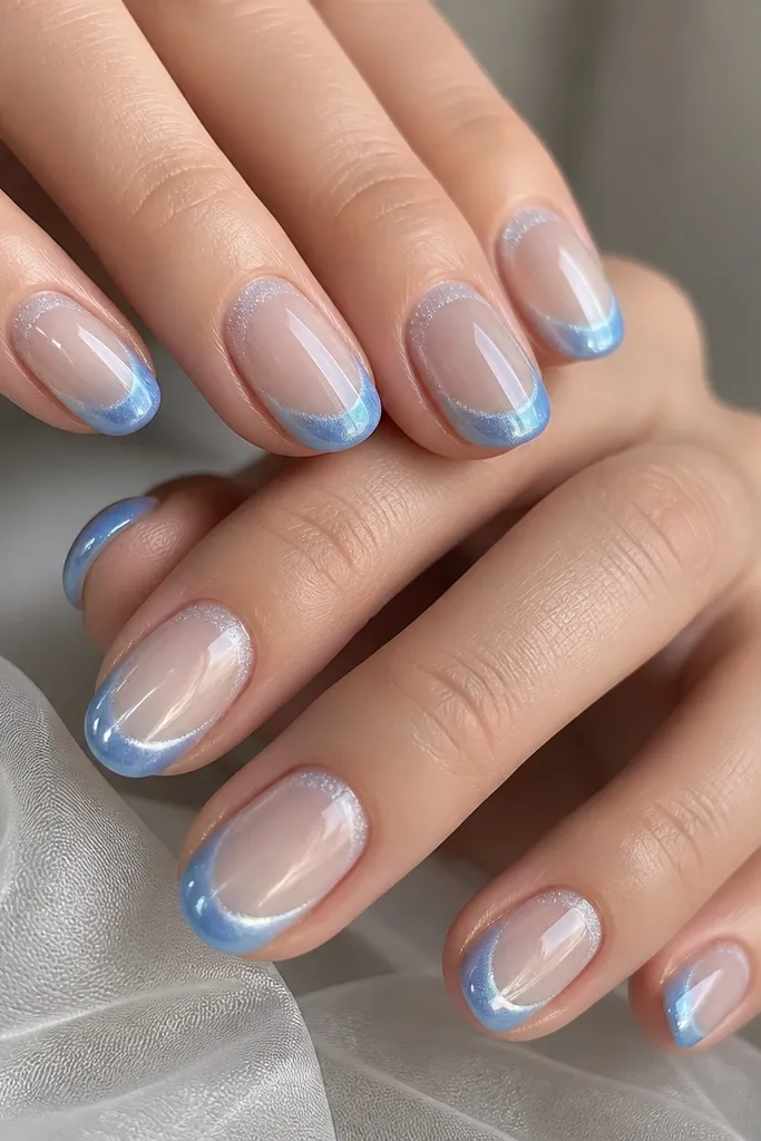 Short oval nails with a frosted nude edge effect near the cuticle. French tips are glacier blue cat eye with a bright streak, and the tip outline is slightly softened like frost. Everything is glossy and clean.