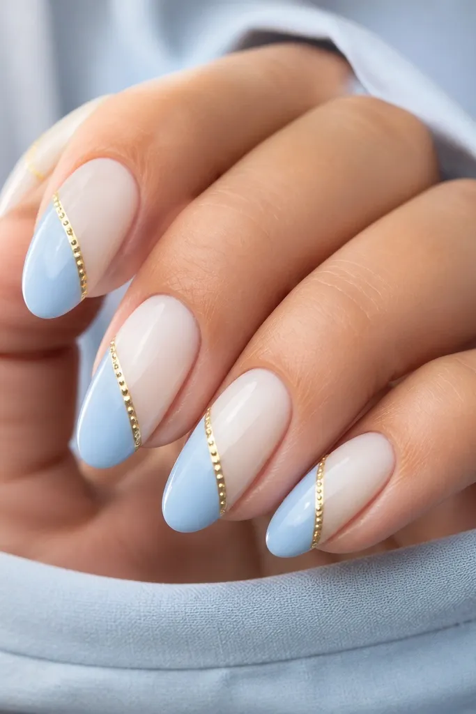 Medium oval nails split by a diagonal sash: lower left is pale blue, upper right is milky white. A gold pinstripe runs along the sash edge, and tiny white dot lights sit on the gold line.