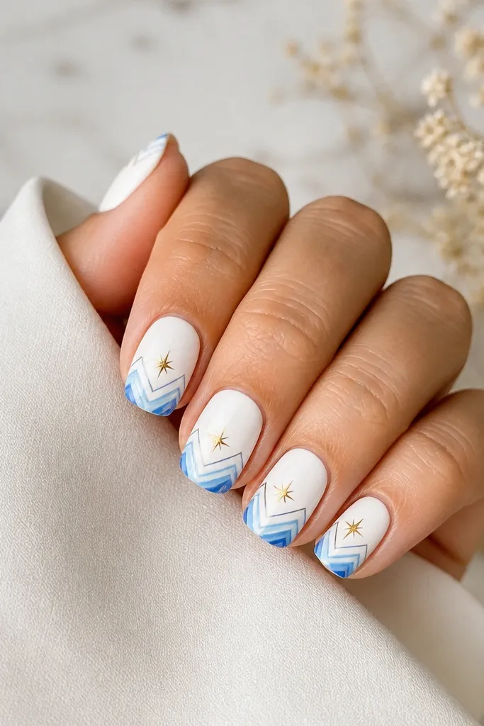 Short-to-medium nails painted glossy white. Blue ombre chevrons sit from the center toward the sides, and gold spark points appear at the chevron tips.
