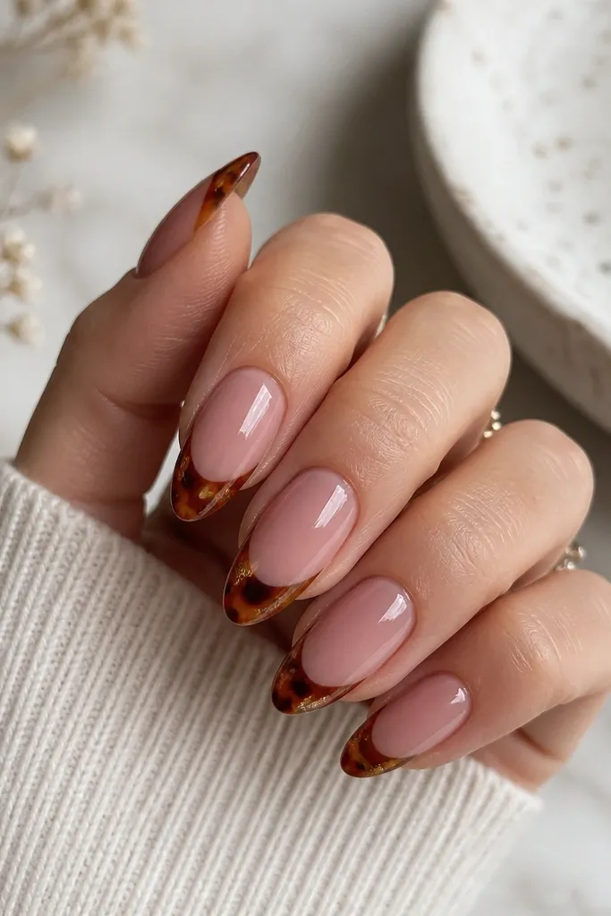 Medium-length almond nails with a nude mauve base; tortoise shell pattern appears only on the tips in burgundy, caramel brown, and tiny gold flecks; high shine.