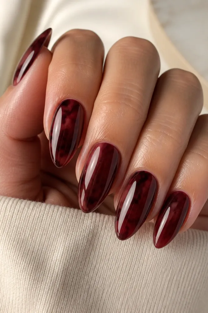Almond nails showing a burgundy tortoise marbling background; one nail has a thicker dark burgundy vein through the center; glossy finish.