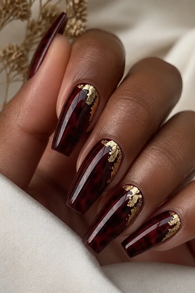 Coffin nails in deep burgundy with tortoise swirls; gold foil pieces sit at the upper corners near the sidewalls; mirror-like shine.