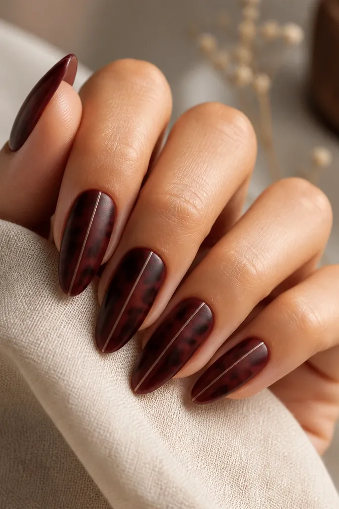 Almond nails with matte burgundy tortoise pattern; one thin glossy stripe runs down the center of each nail; soft matte glow.