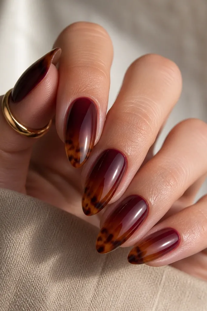 Medium almond nails with a burgundy-to-warm-brown ombre; tortoise swirls concentrate near the tips; glossy finish.
