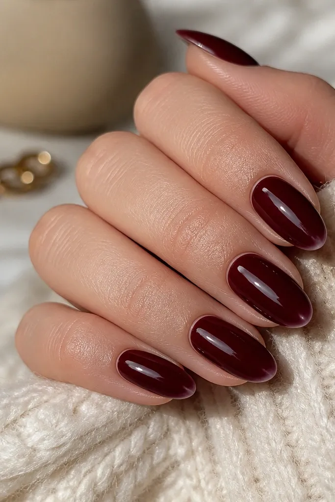 Almond nails painted a deep burgundy wine color, with a super glossy finish. The tip edges look extra bright from light reflection.