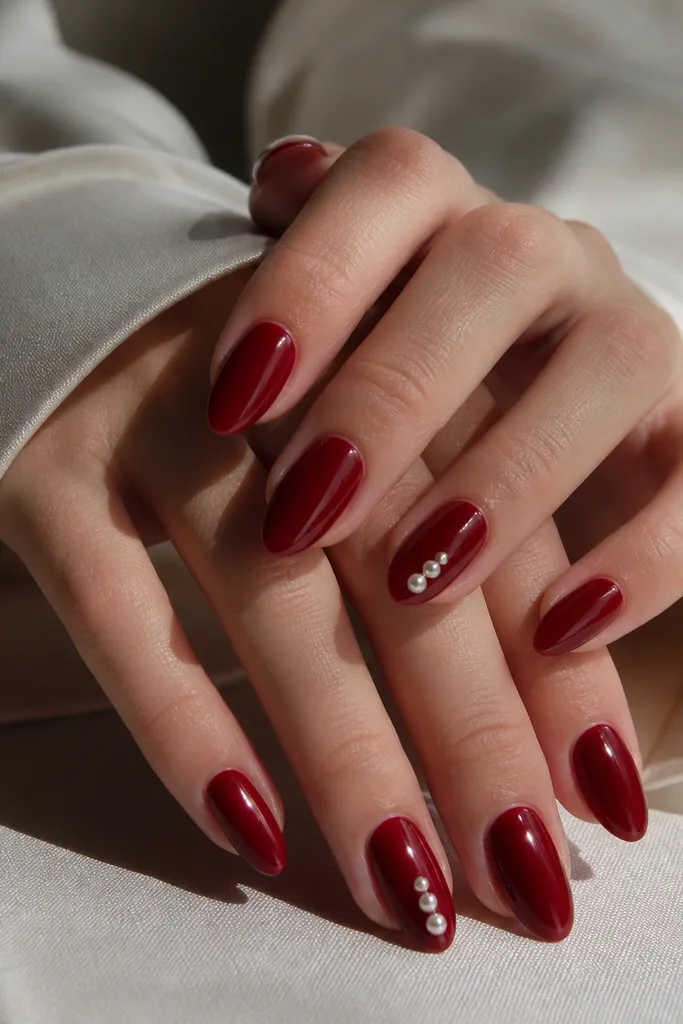 Deep glossy red nails. Two nails have tiny pearl studs placed in a vertical line near the tip, while the rest of the nails stay plain red with a clean shine.