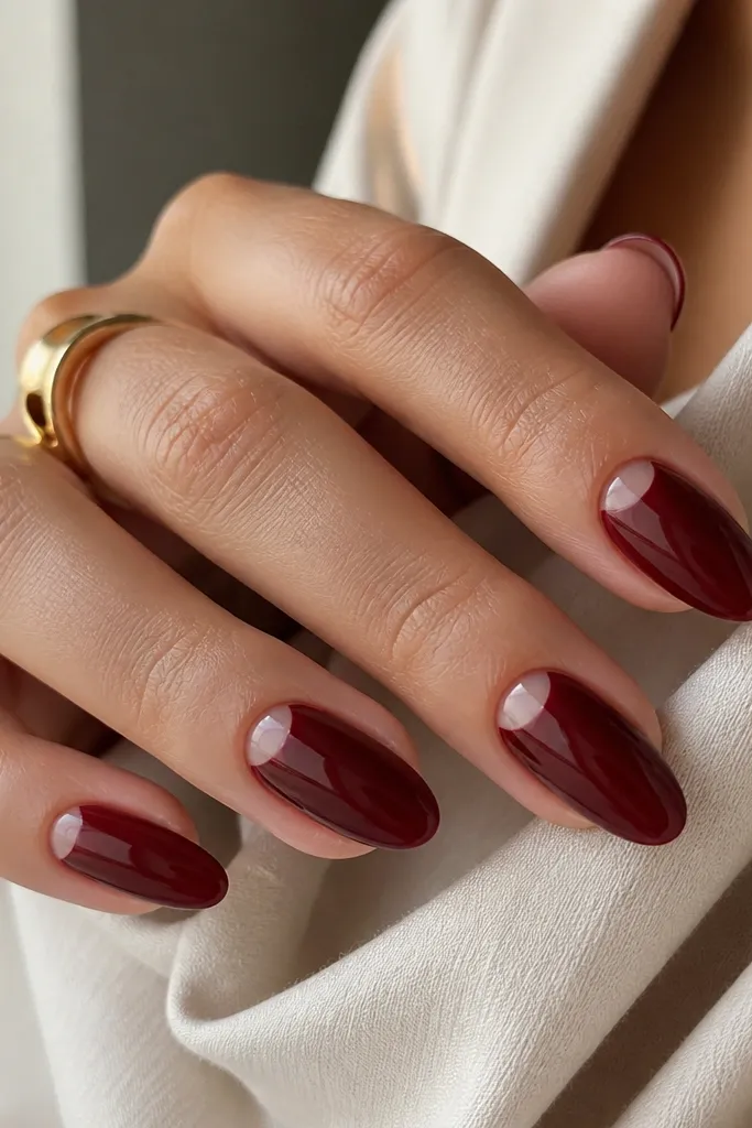 Medium-length almond nails in deep wine red with a crisp negative-space half-moon near the cuticle on each nail; the rest is solid gloss red.