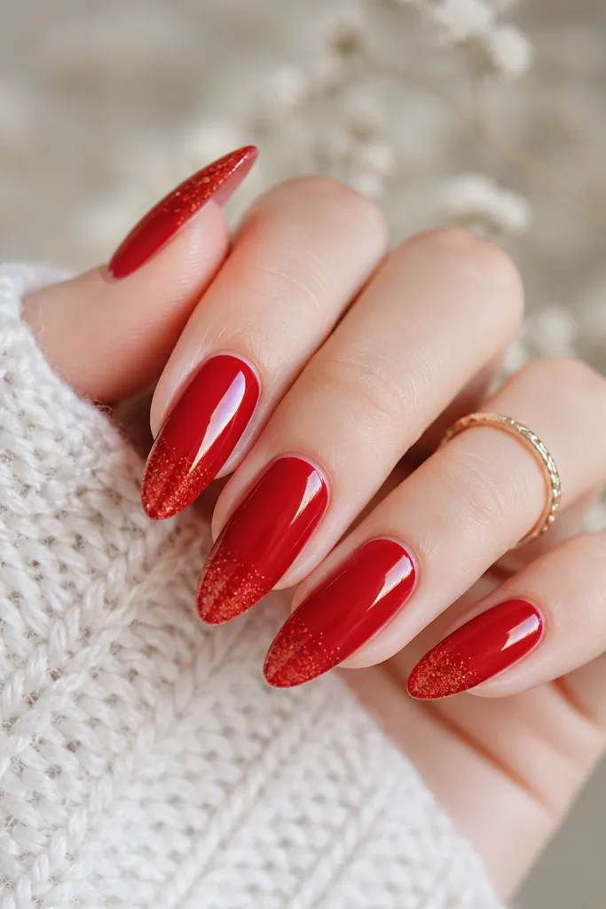 Long almond nails painted crimson red with micro-glitter concentrated only on the tips; the base is solid glossy red, glitter fades upward slightly.