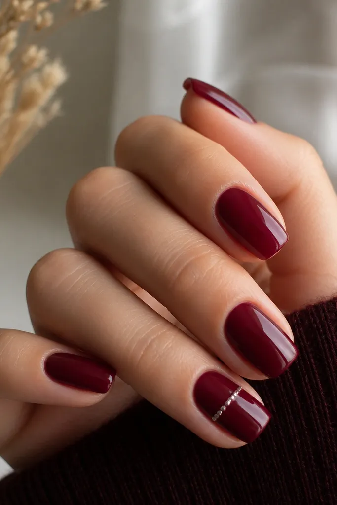 Deep wine red nails with one accent nail featuring a thin straight line of tiny silver micro-studs running horizontally across the middle; rest is plain glossy red.