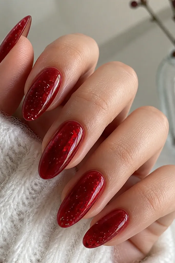 Medium almond nails painted translucent red like stained glass; topped with clear gloss and a few tiny silver specks suspended under the gel.