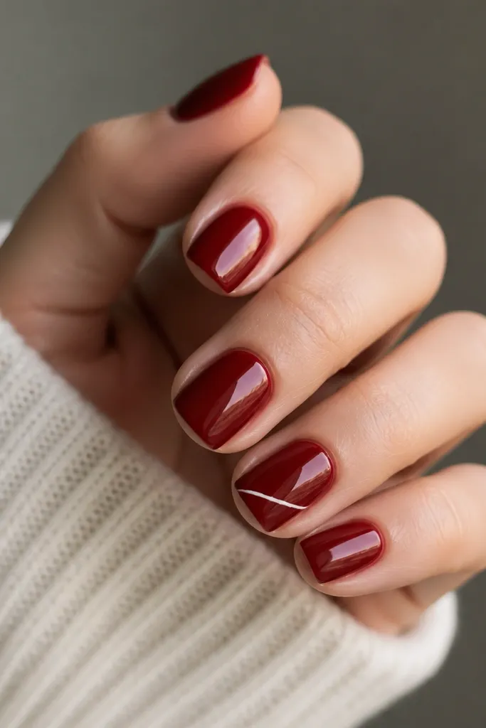 Short squoval nails in glossy crimson; one nail has a single thin white micro-line running diagonally near the tip, like a fine pen stroke.