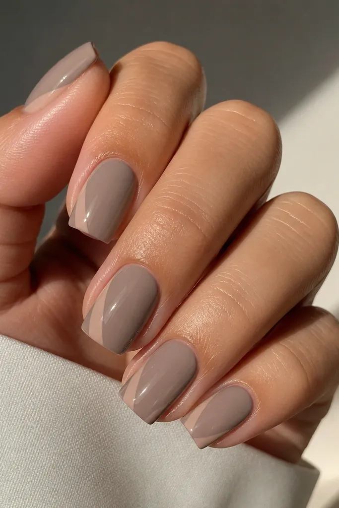 Icy taupe square nails with a glossy finish. On each nail, there's a thin nude line that sweeps diagonally from the lower sidewall toward the center, stopping before the tip. The rest of the nail is solid taupe, with clean, crisp edges.